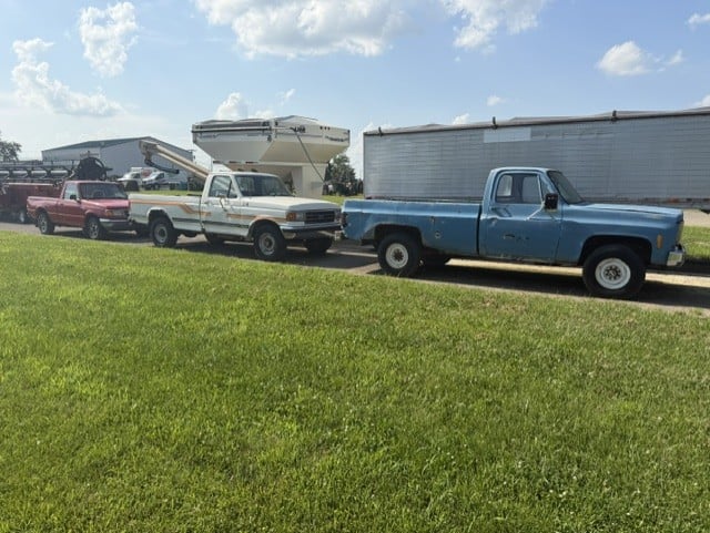 Blue and white pickup trucks parked beside grain hopper wagon